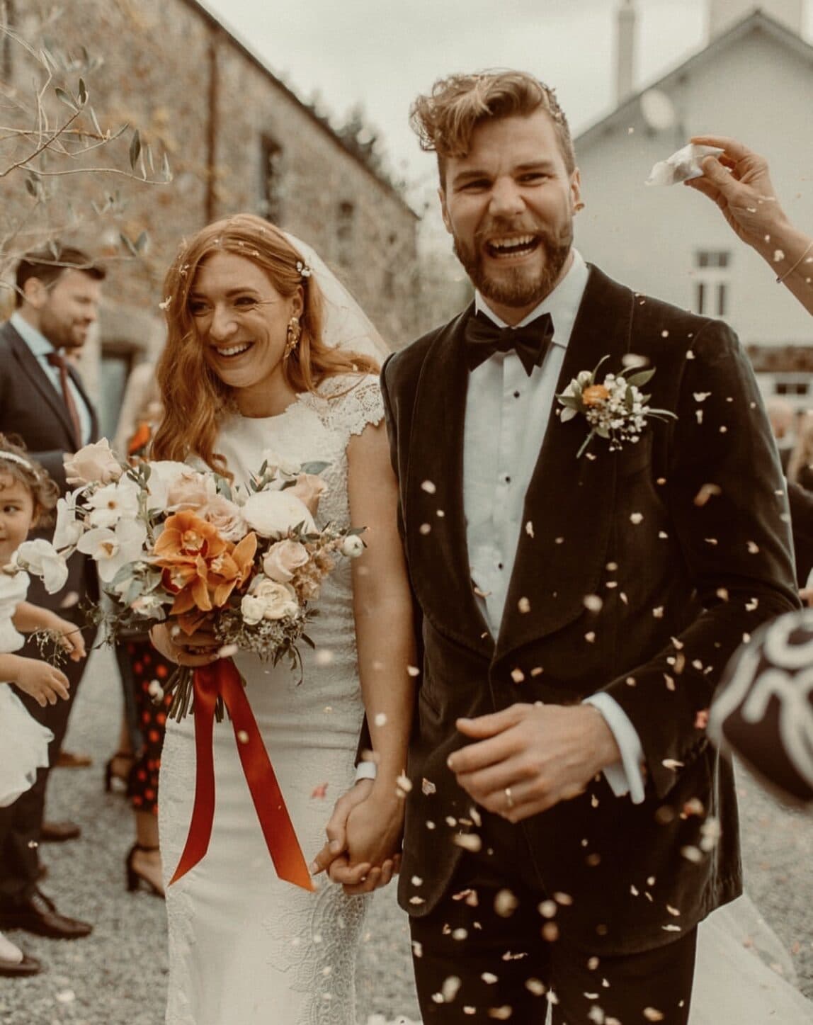 Red-haired bride and groom laughing under confetti