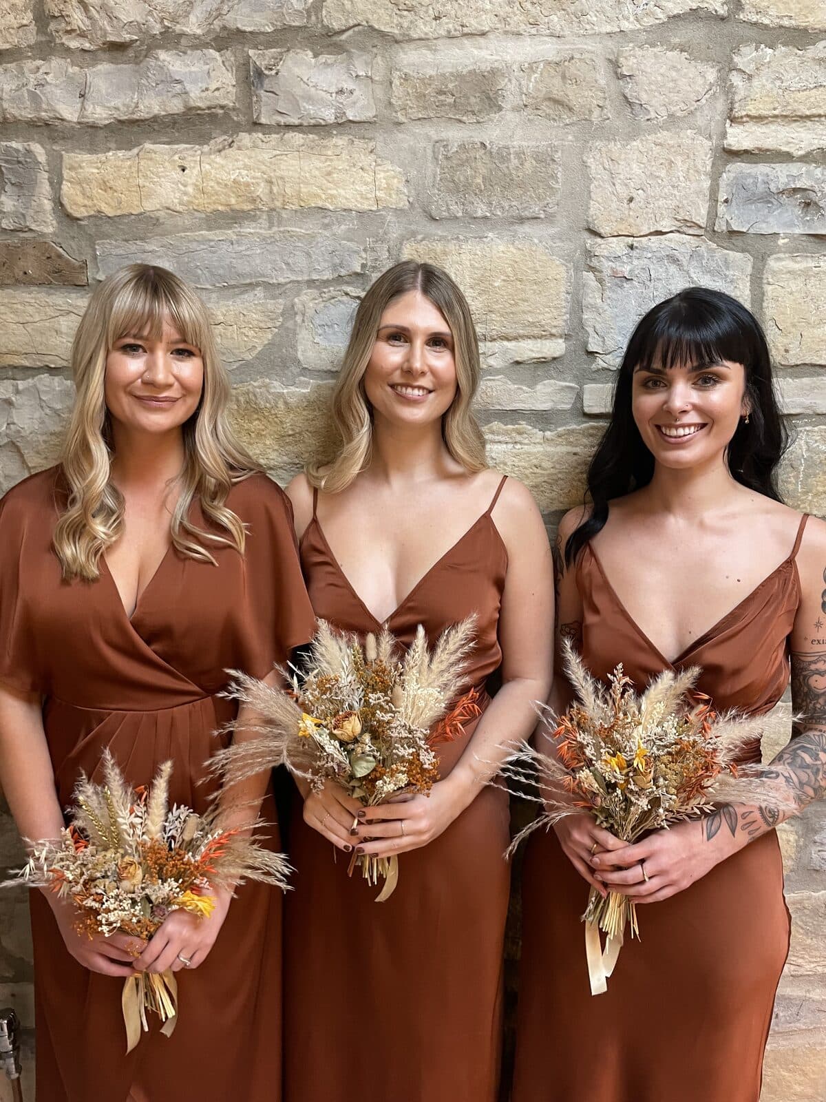 Three bridesmaids in rust satin holding dried bouquets