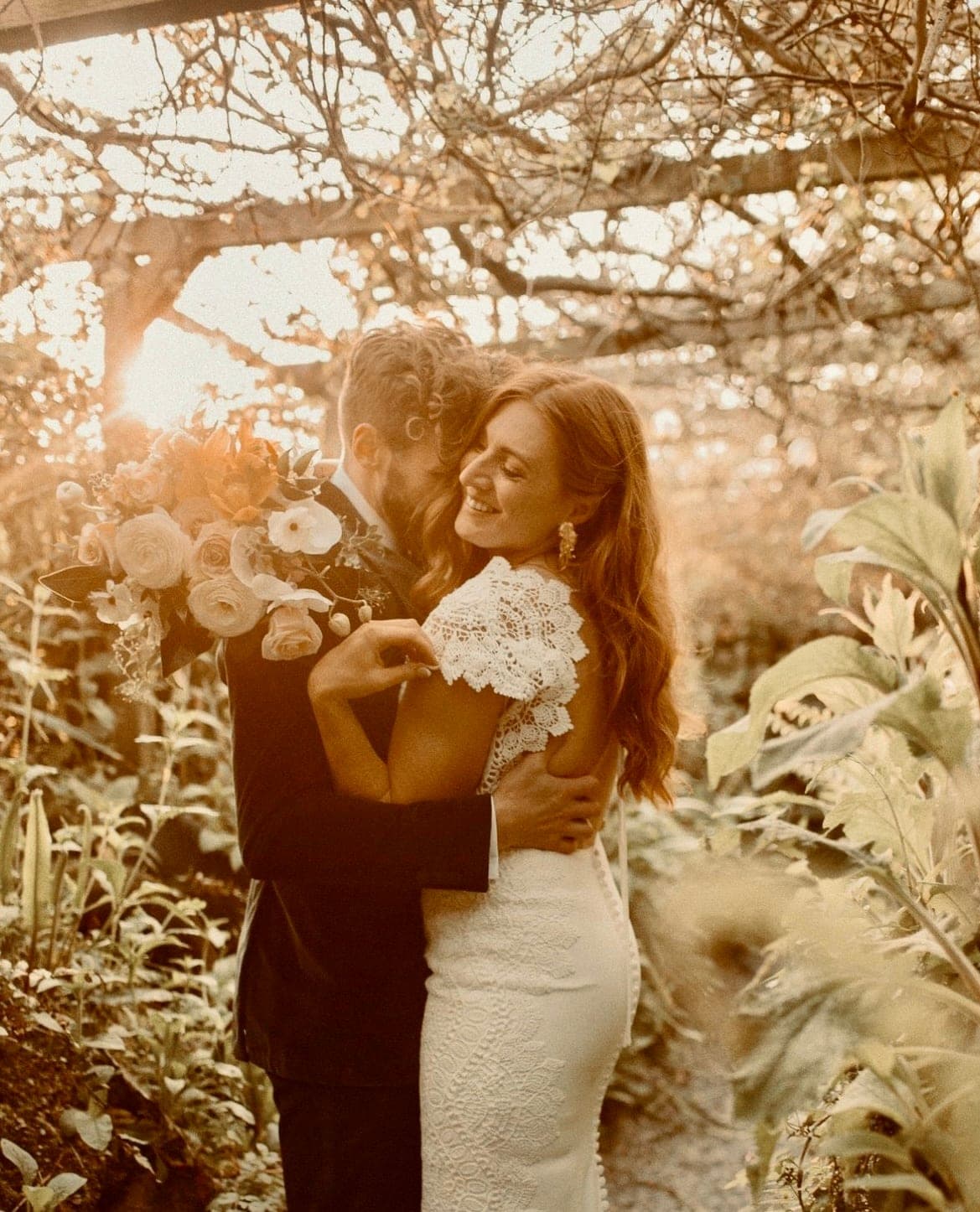 A bride and groom embracing in a sunlit glasshouse